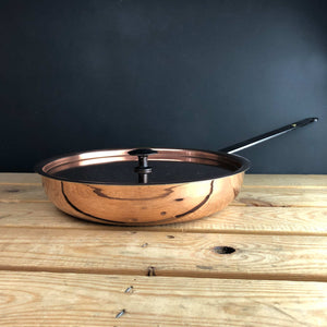 Copper frying pan with lid on table