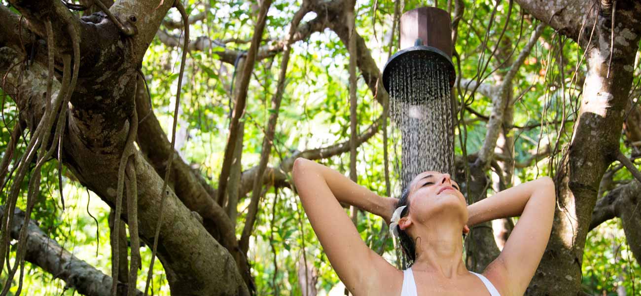 Woman taking a shower outside in woodland setting 