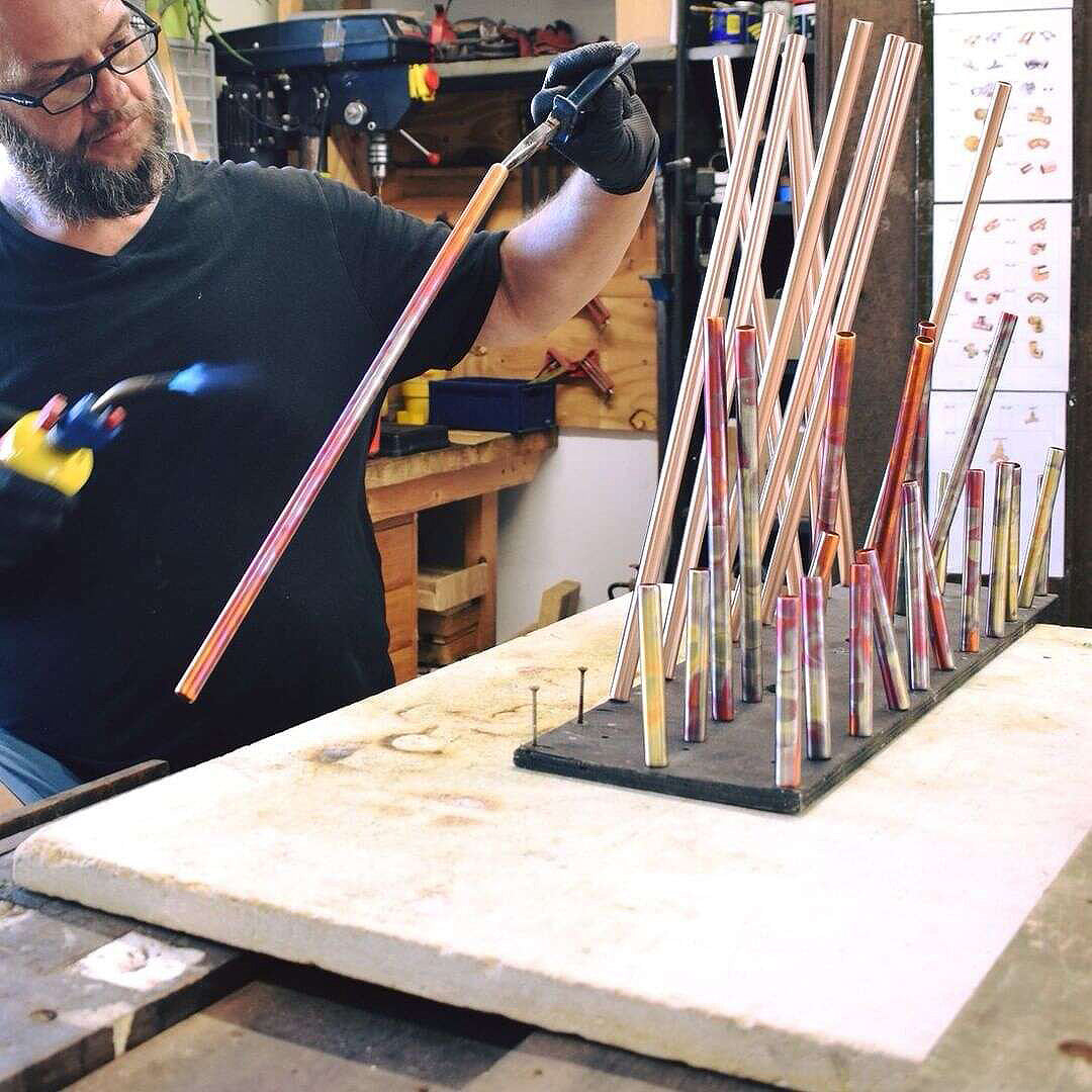 male blowtorching copper pipe to marbled design 