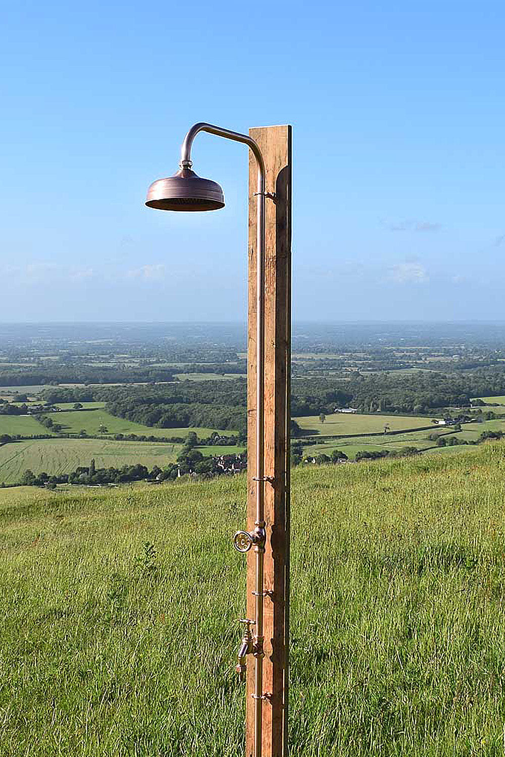 a fully copper outside shower photographed next to a stunning view of Brighton countryside 