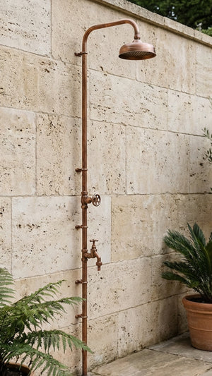Outdoor shower system mounted on a stone wall with plants around.