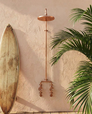 Copper shower system mounted on a textured wall with a surfboard and plant in the background.