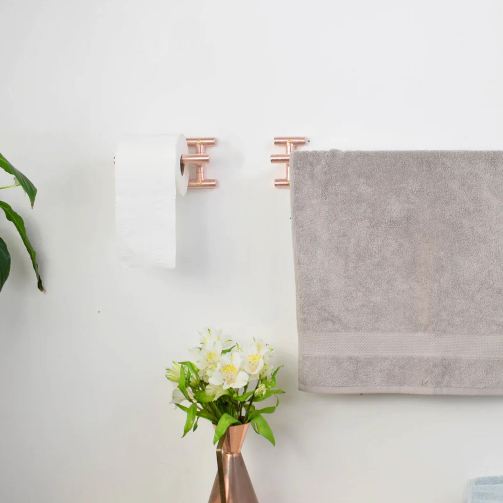 Gray towel hanging on a rose gold rack with a vase of flowers on a white wall.