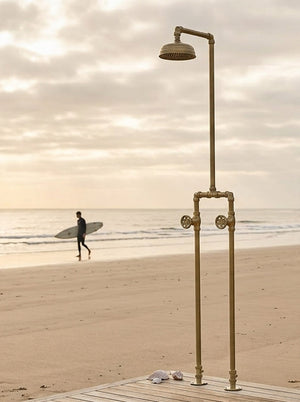 Outdoor shower -free standing on a wooden platform with a beach and person with a surfboard in the background