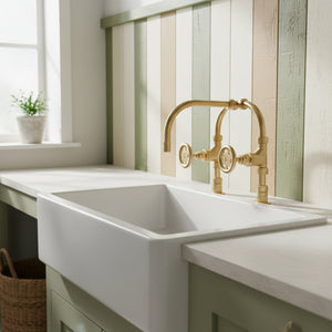 White kitchen sink with gold faucet in a bright room with striped wallpaper.