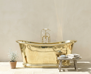 brass bathtub in a bathroom setting with a small table and plant.
