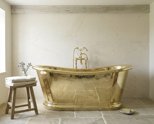 brass freestanding bathtub in a bathroom with a wooden stool and towels.