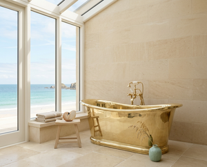 brass bathtub in a luxurious bathroom with large windows overlooking the ocean.