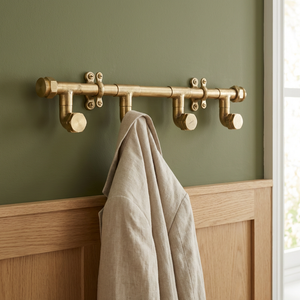 Brass pipe-style hook rack on a green wall with a beige towel draped over it.