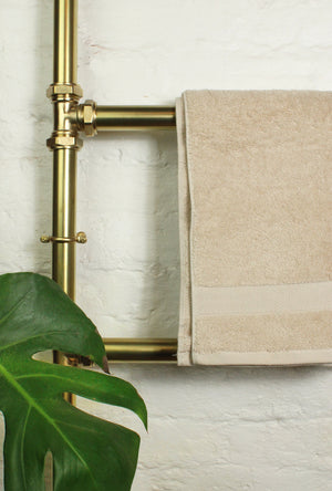 Beige towel hanging on a gold towel rack against a white brick wall with a green leafy plant.