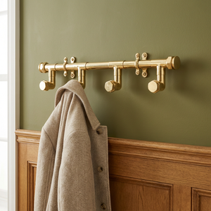 brass coat rack with hooks against a green wall with a coat hanging on it.