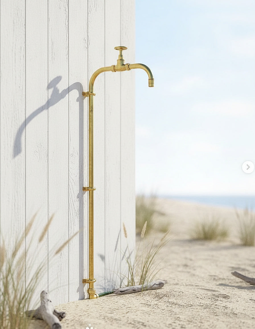 Brass outdoor tap mounted on a white wall with sand and grass in the background