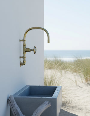 Vintage-style brass wall-mounted faucet on a concrete sink with a beach background