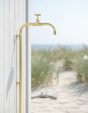 brass garden tap mounted on a wall with a beach background