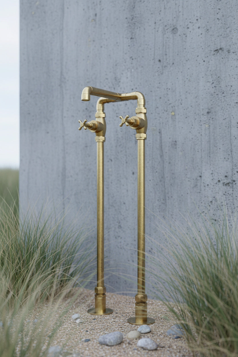 Brass outdoor tap wash against a concrete wall with grass and stones in the foreground.