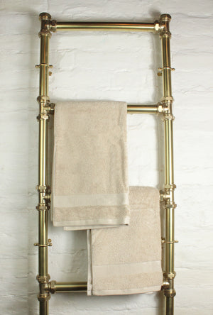 Brass towel rack with beige towels on a white tiled wall