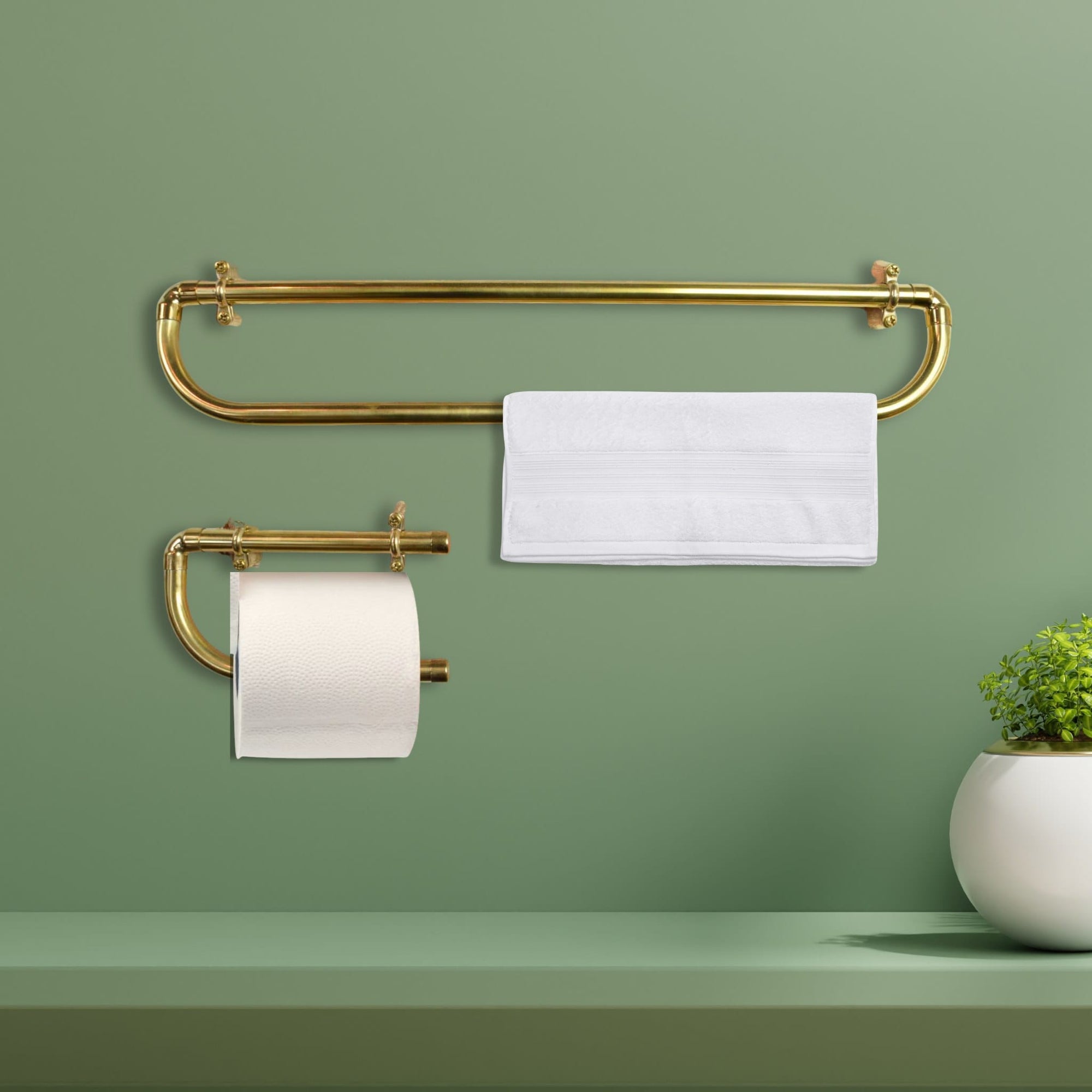 brass towel rack with a white towel and toilet paper holder against a green wall.