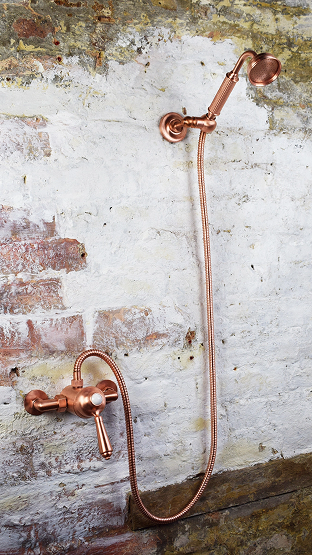 copper mixer with handheld shower and flexible hose photographed on a brick wall