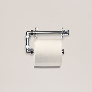 Metallic toilet paper holder with a roll of toilet paper on a light gray background