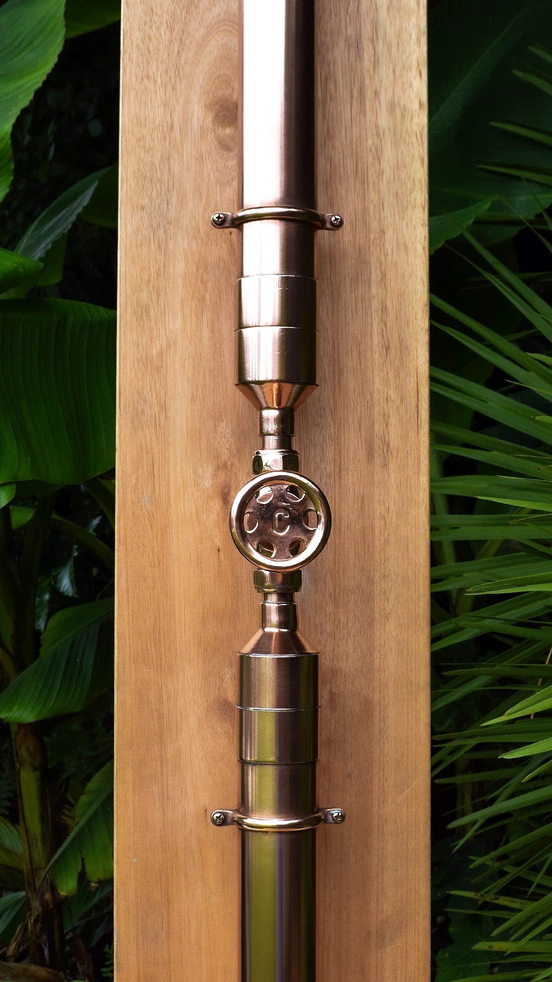 Copper shower valve on surfboard against green backdrop