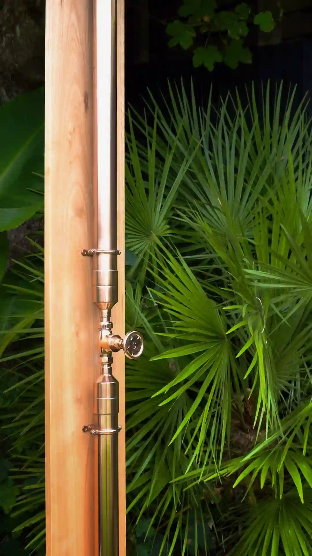 copper shower on surfboard against green plants 