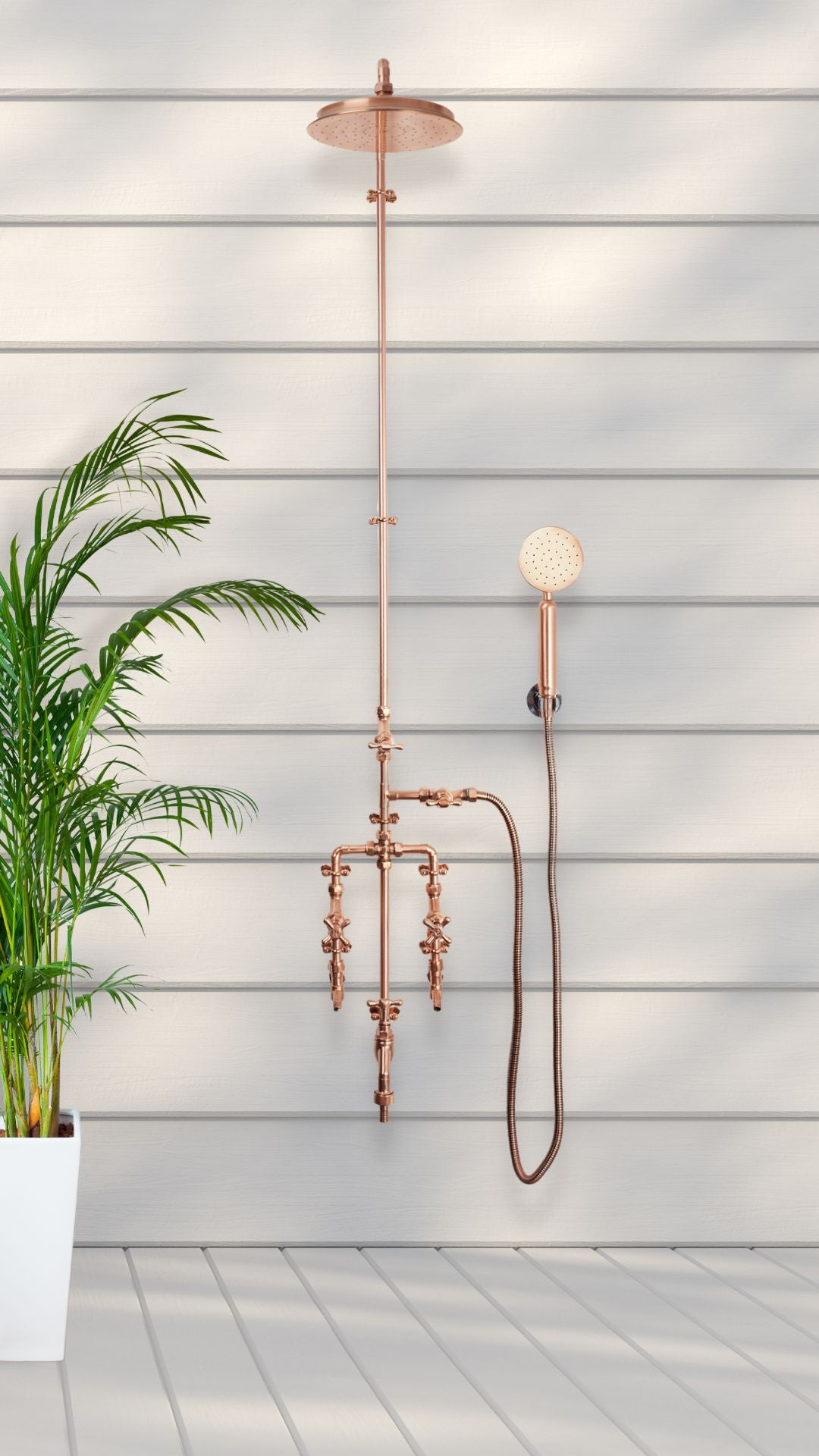 copper garden shower featured outside on a white decking, wall mounted on the side of the house, on a cladded wall