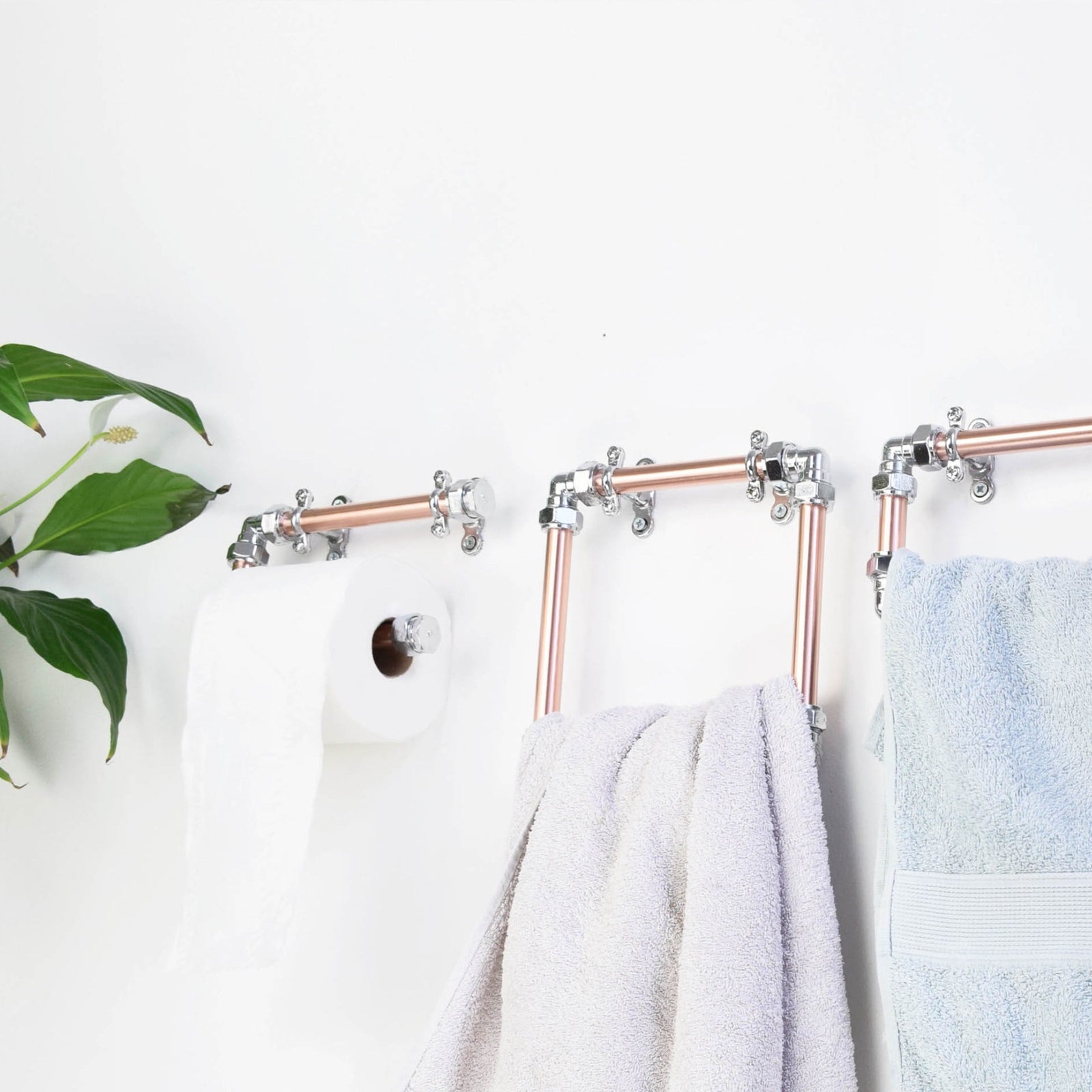 Towel rack with copper pipes and hooks holding towels on a white wall.