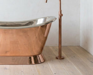 Copper bathtub with a standing faucet on a wooden floor.