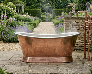 Copper bathtub in a garden setting with flowers and stone wall.