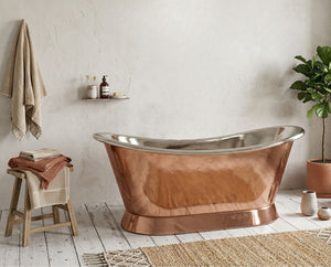 Copper bathtub in a bathroom with a plant and stool.