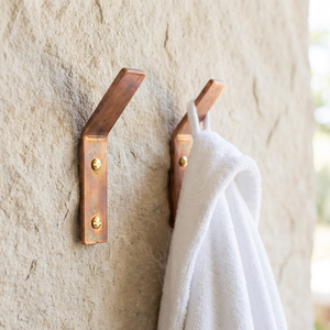 Two copper hooks on a stone wall with a white towel hanging from one of them.