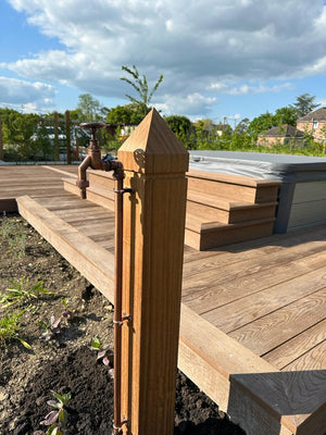 Wooden post with a garden faucet on a wooden deck with trees and buildings in the background