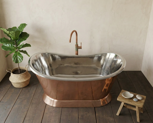 Copper bathtub with a plant and small stool in a room with wooden floor and beige walls.