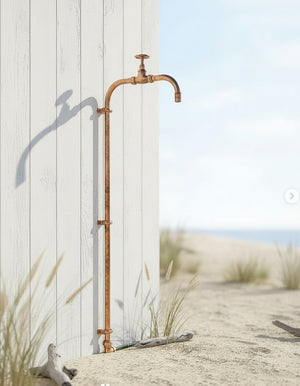 Copper outdoor tap and hose on a sandy beach with grasses and driftwood