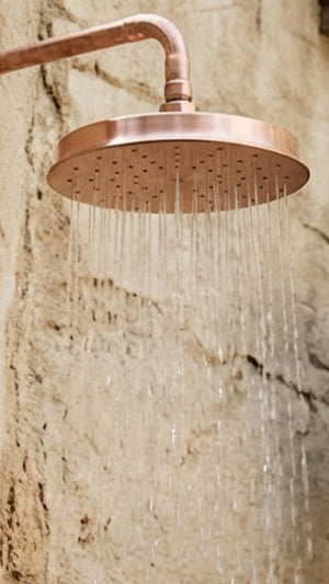 Copper shower head with water droplets against a stone wall background