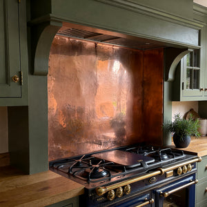 Stainless steel range with copper backsplash in a heritage kitchen setting