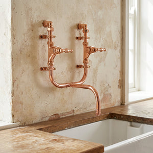 Copper kitchen tap on a textured wall above a bathtub.