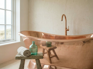 Copper bathtub in a bathroom with wooden stools and bottles.