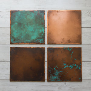 Four copper tiles with different textures and colors on a light wooden surface.