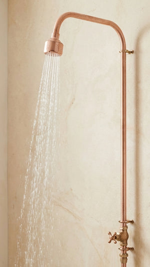 Copper shower head and fixture on a beige wall