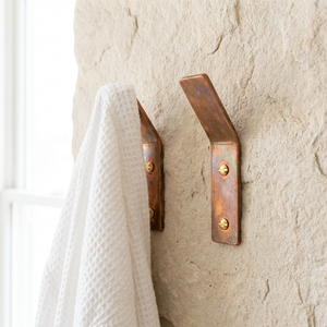 Two copper hooks on a textured wall with a white towel hanging from one of them.