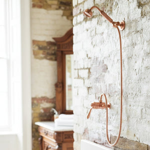 Copper shower head and hose mounted on a textured stone wall.