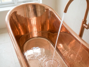 Copper bathtub with water flowing into it, set against a neutral background.