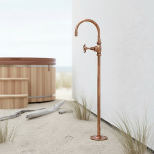 Copper outdoor faucet on a sandy background with a wooden hot tub.