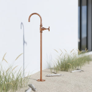 Copper outdoor faucet on a sandy beach with grasses and a building in the background