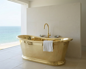 brass bathtub with a white towel in a bathroom with a window view of the ocean.