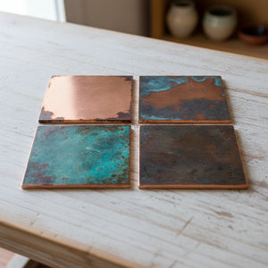 Four square metal tiles with different finishes on a wooden surface