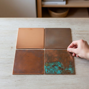Four copper tiles with varying finishes on a wooden surface.