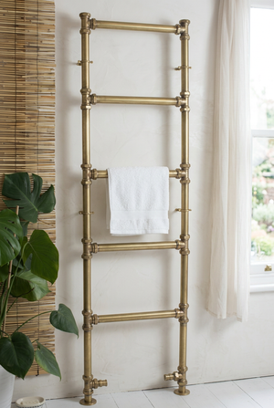 Brass towel ladder with a white towel against a white wall.