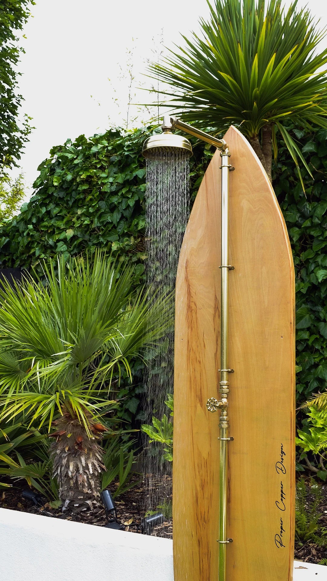 Wooden surfboard with a shower head against a green outdoor background